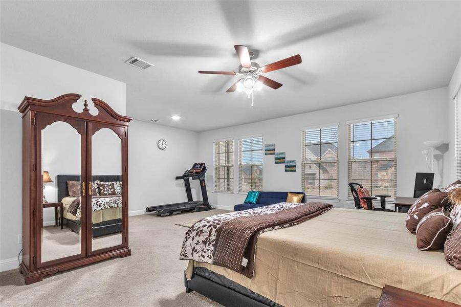 Carpeted bedroom with ceiling fan, visible vents, and baseboards