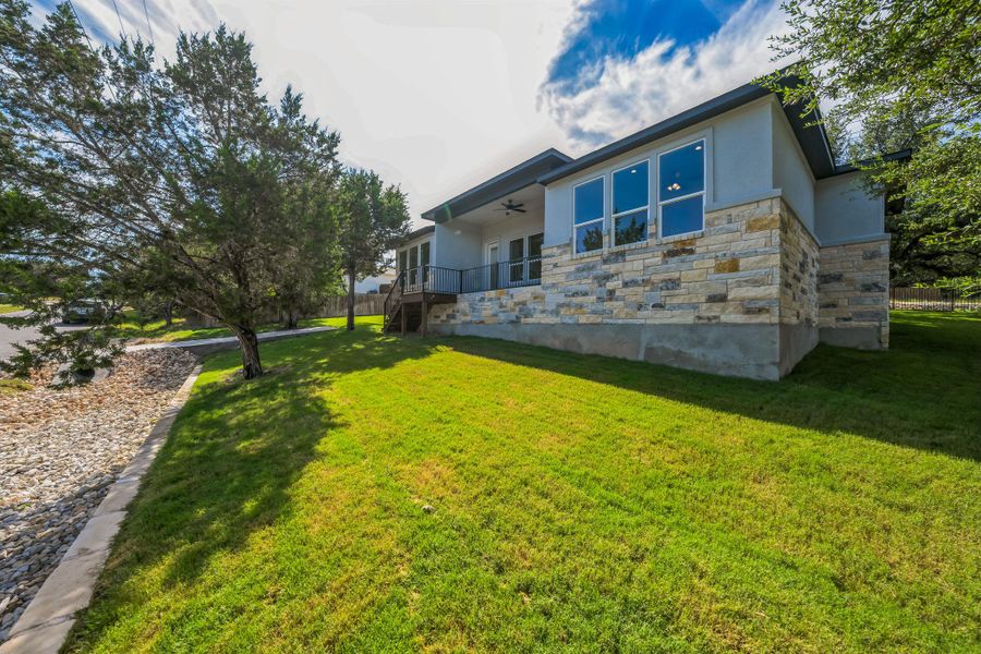 Back of property with stone siding, stucco siding, a ceiling fan, a lawn, and stairway