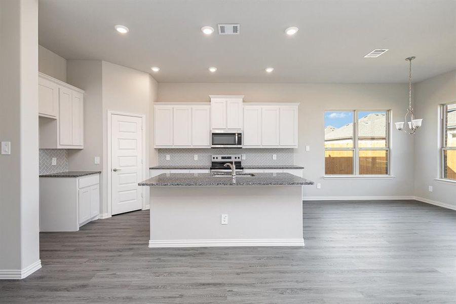 Kitchen with a center island with sink, hardwood / wood-style flooring, white cabinetry, and appliances with stainless steel finishes