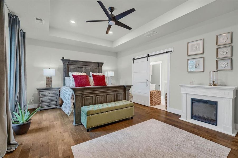 Bedroom featuring dark hardwood / wood-style floors, ceiling fan, a barn door, and a raised ceiling