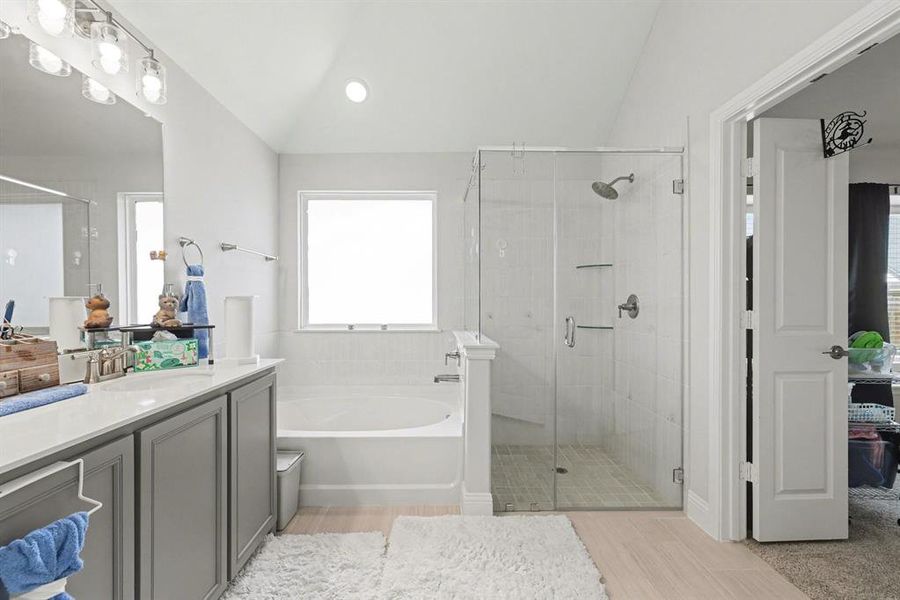 Contemporary bathroom featuring a spacious glass-enclosed shower, separate soaking tub with tiled surround, and a dual-sink vanity with light-colored countertops and gray cabinetry