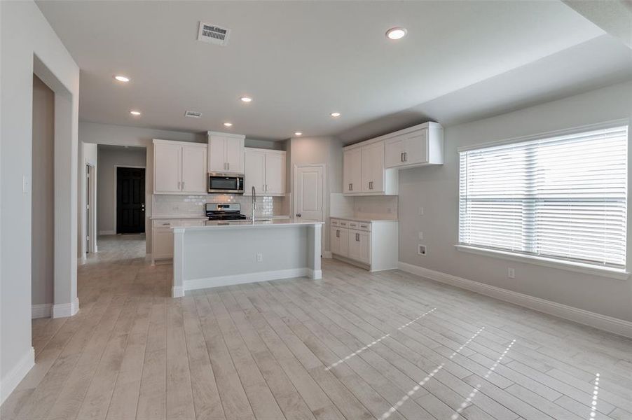 Kitchen with sink, a center island with sink, appliances with stainless steel finishes, and white cabinetry