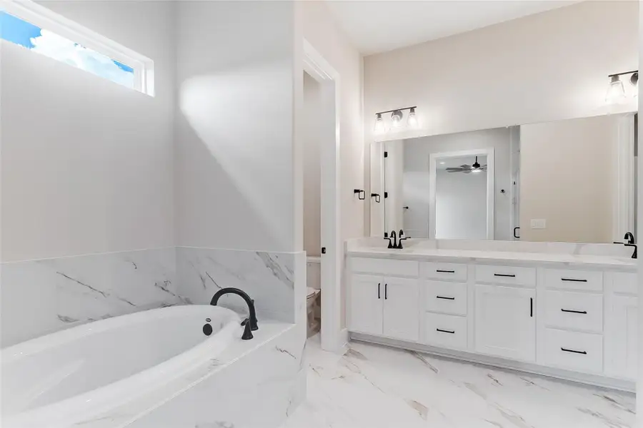 Full bath with double vanity, a bath, light marble finish floors, and ceiling fan