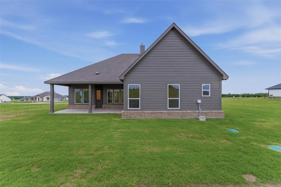 Rear exterior featuring a covered patio with columns, brick skirting, gray horizontal siding, and multiple windows