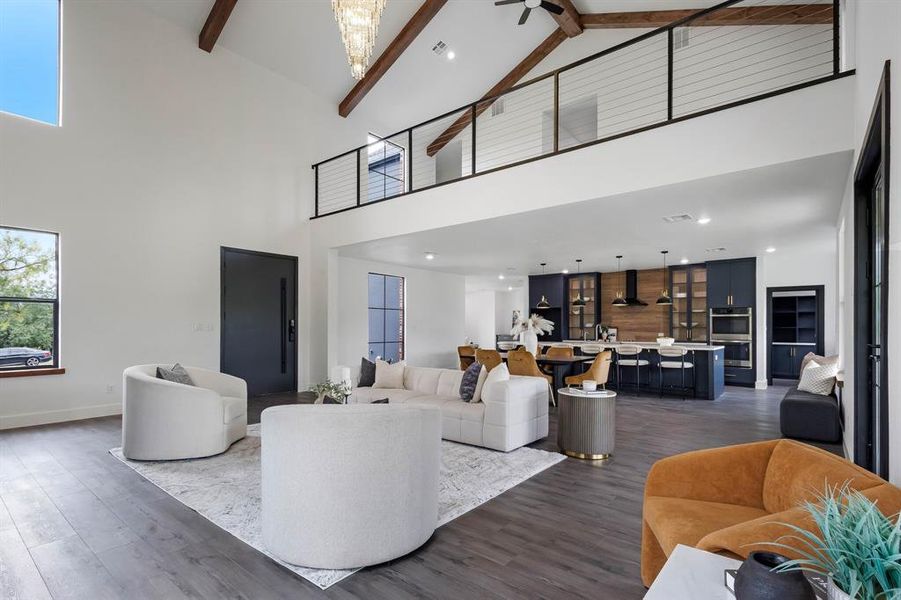 Expansive open-concept living area featuring vaulted ceilings with exposed wood beams, a striking chandelier, and wood-finish flooring Expansive open-concept living area featuring vaulted ceilings with exposed wood beams, a striking chandelier, and wood-finish flooring