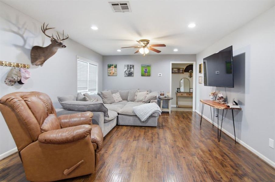 Spacious living area featuring wood-finish flooring, light grey walls, recessed lighting, and a ceiling fan