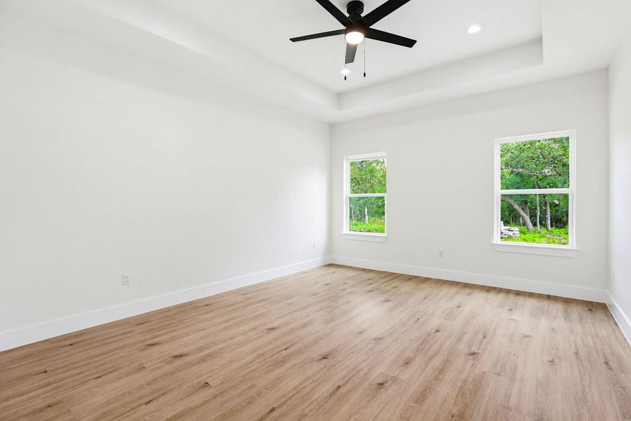 A spacious, airy  primary bedroom features a tray ceiling