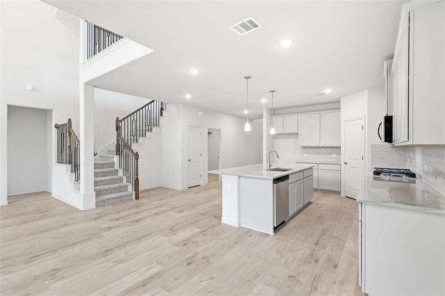 Kitchen with light stone countertops, light wood-style flooring, a center island with sink, decorative light fixtures, and stainless steel appliances
