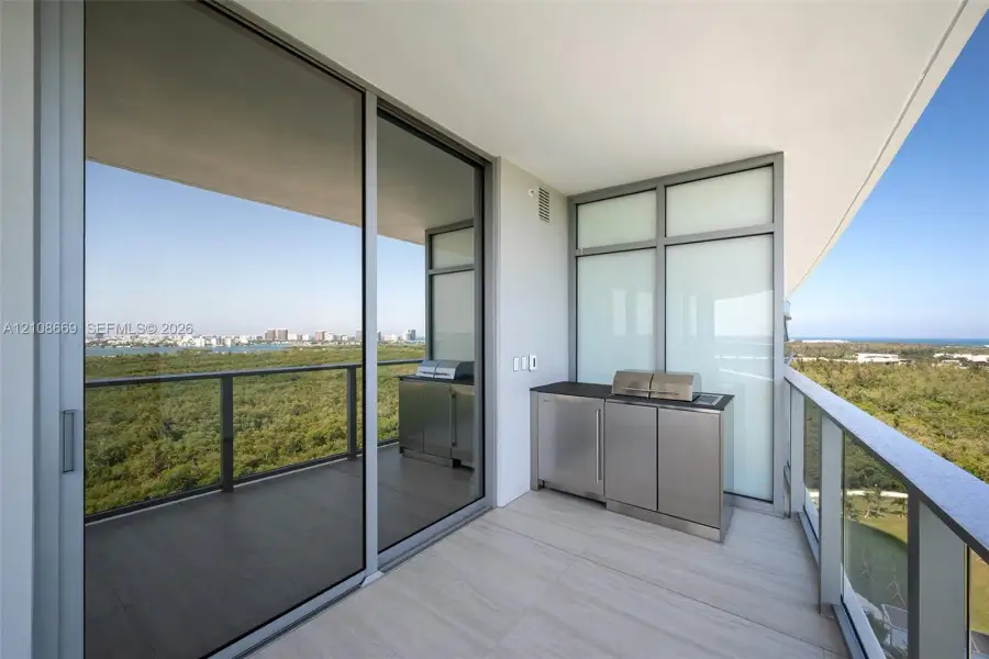 Covered balcony featuring tile flooring, metal railing, built-in stainless steel outdoor kitchen cabinetry, and expansive glass sliding doors