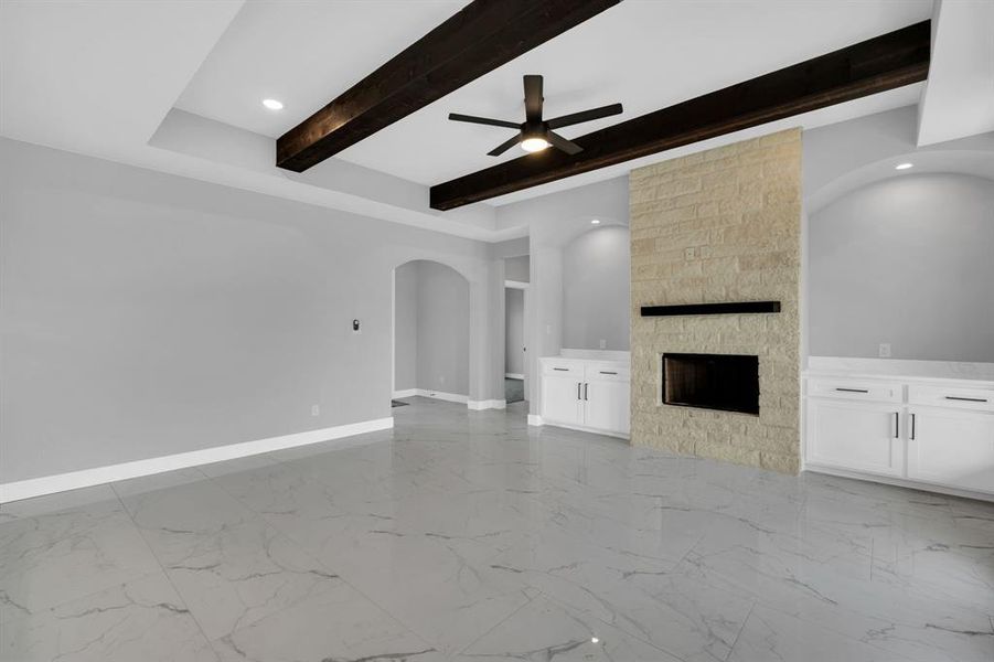 Unfurnished living room featuring ceiling fan, a stone fireplace, beam ceiling, and light tile patterned floors