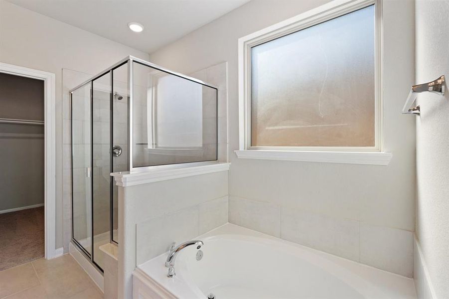 This additional view of your primary bathroom features tile flooring, fresh paint, walk-in shower, a separate garden tub, and a large walk-in closet.