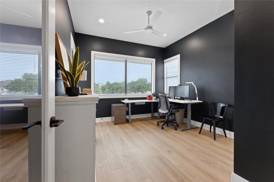 Well-lit interior space featuring expansive windows, wood-finish flooring, a contemporary ceiling fan, recessed lighting, and dark accent walls Well-lit interior space featuring expansive windows, wood-finish flooring, a contemporary ceiling fan, recessed lighting, and dark accent walls