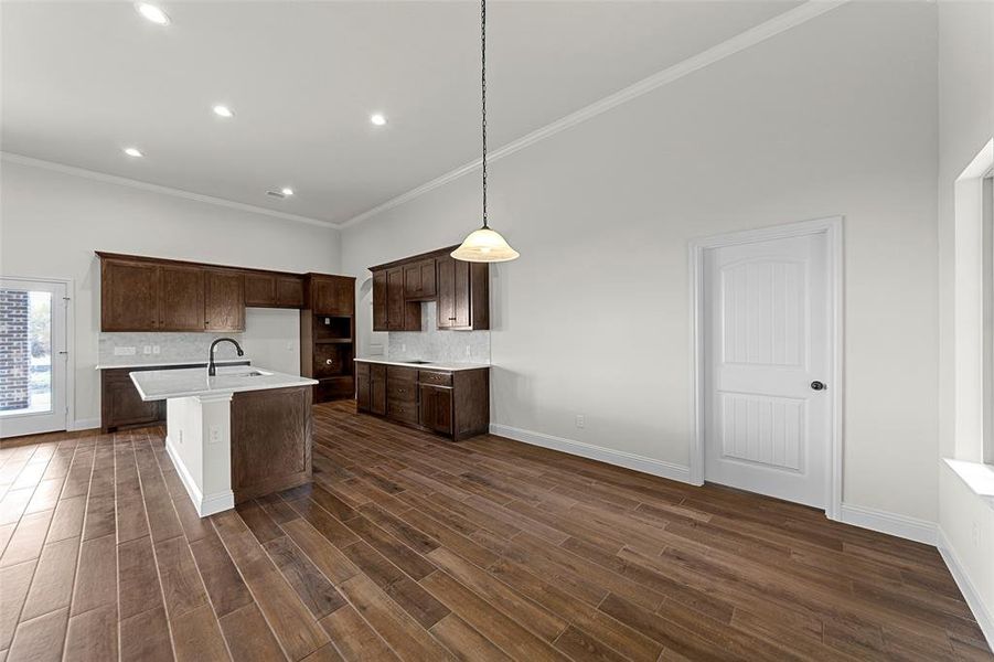 Kitchen with dark hardwood / wood-style flooring, a center island with sink, decorative light fixtures, and ornamental molding