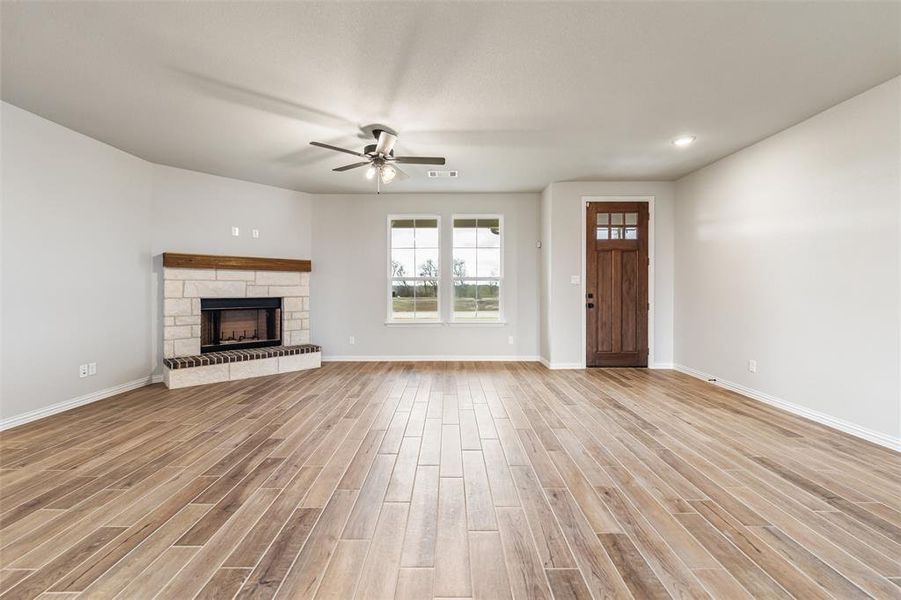 Unfurnished living room featuring light wood-style flooring, a fireplace, and ceiling fan Unfurnished living room featuring light wood-style flooring, a fireplace, and ceiling fan