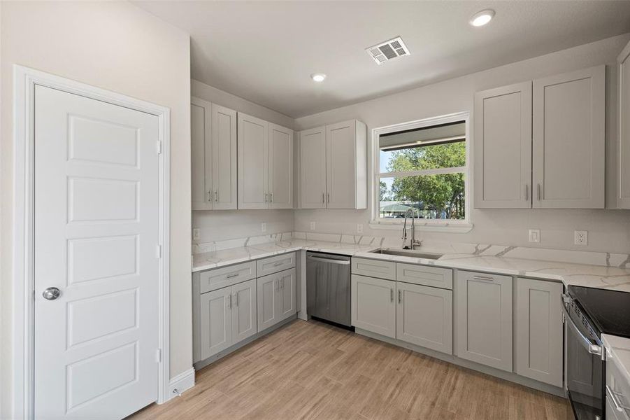 Kitchen featuring range, light hardwood / wood-style flooring, stainless steel dishwasher, sink, and gray cabinetry