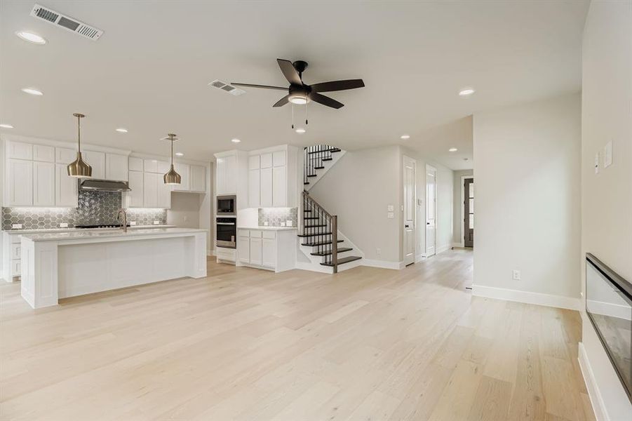 Unfurnished living room with a ceiling fan, stairs, light wood-type flooring, and recessed lighting