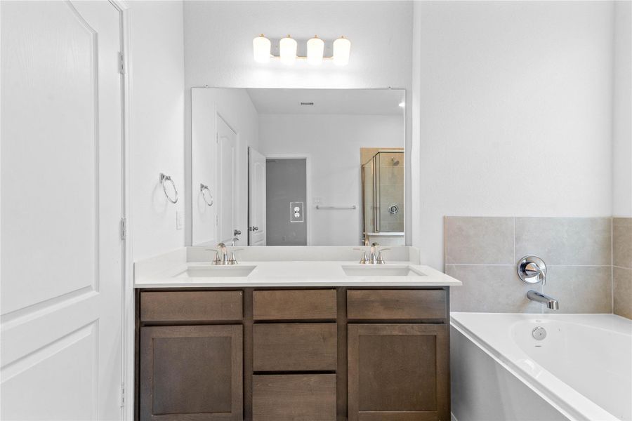 This beautifully updated primary bathroom is move-in ready! It showcases stained cabinetry paired with light countertops, dual vanity sinks, a large framed mirror, a spacious walk-in closet with built-in shelving, high ceilings, custom paint, and stylish modern finishes throughout.