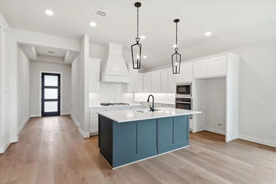 Designer kitchen featuring a large island, quartz countertops, and stylish two-tone cabinetry with modern pendant lighting.