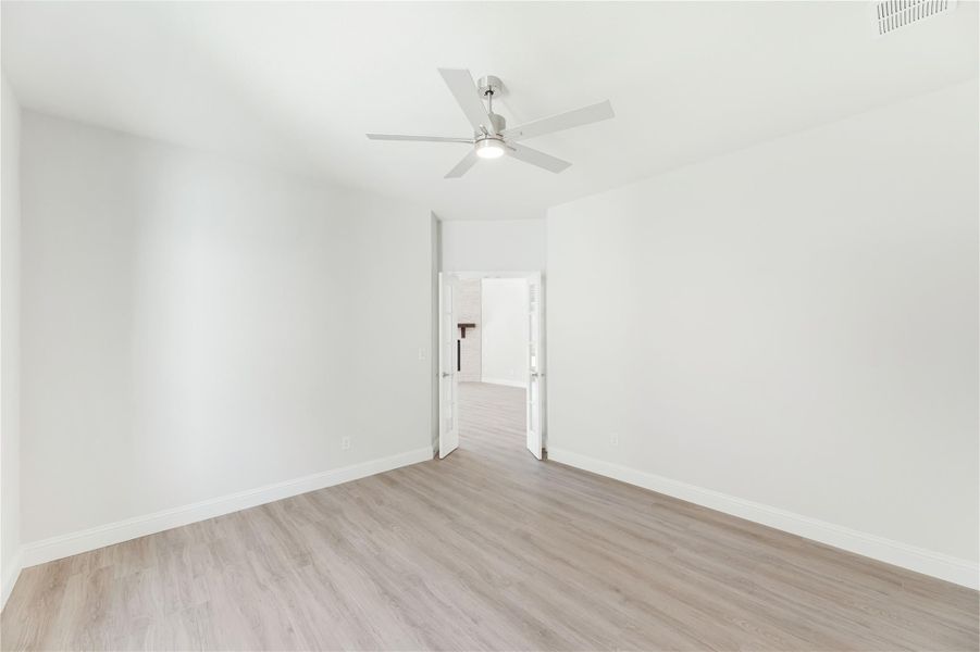 Empty bedroom with light wood floors, white walls, and a ceiling fan with light fixture