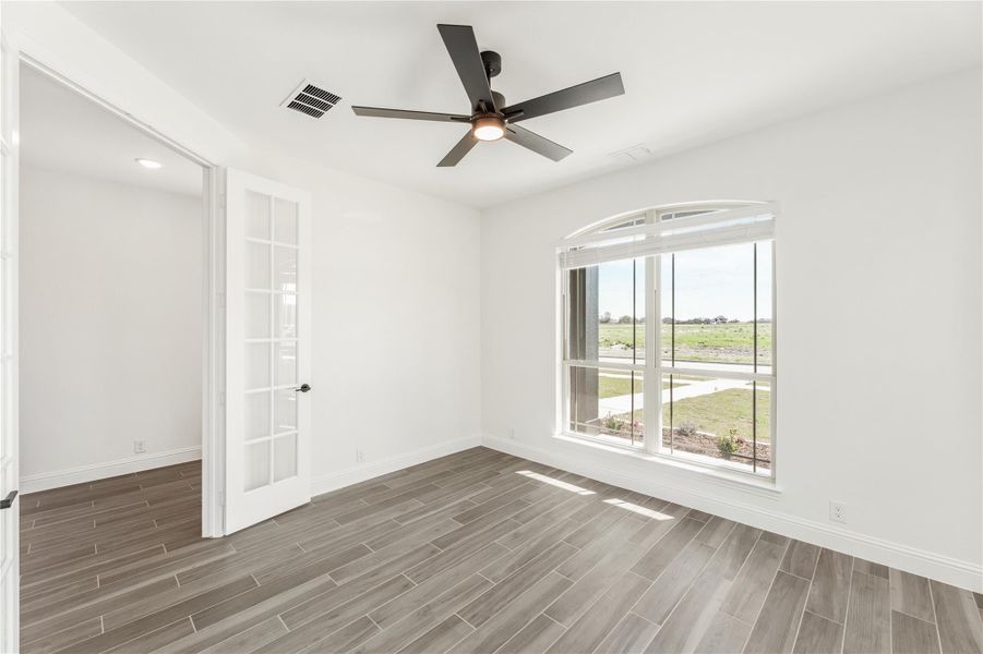 Empty room with wood-look tile floors, ceiling fan, arched window, and French door Empty room with wood-look tile floors, ceiling fan, arched window, and French door