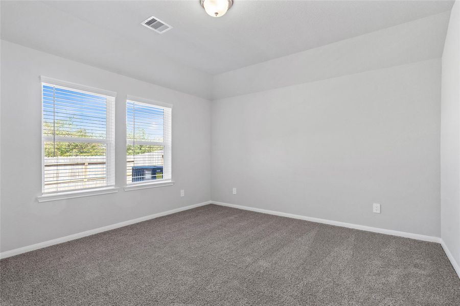 The primary bedroom provides a peaceful escape with a bright, neutral palette, sloped ceilings, large windows, and plush carpet flooring, creating a calm and restorative atmosphere to end your day.