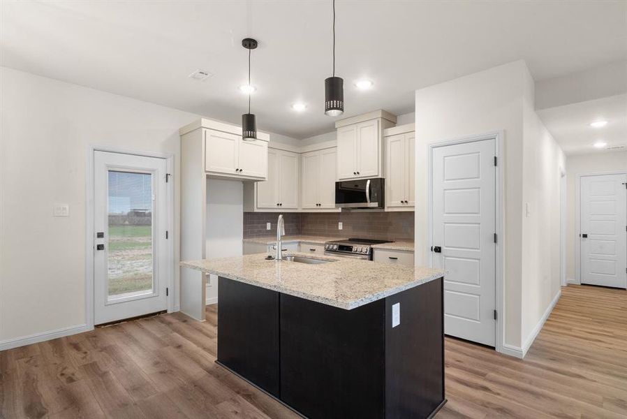 Kitchen with white cabinetry, light stone countertops, pendant lighting, a kitchen island with sink, and appliances with stainless steel finishes Kitchen with white cabinetry, light stone countertops, pendant lighting, a kitchen island with sink, and appliances with stainless steel finishes