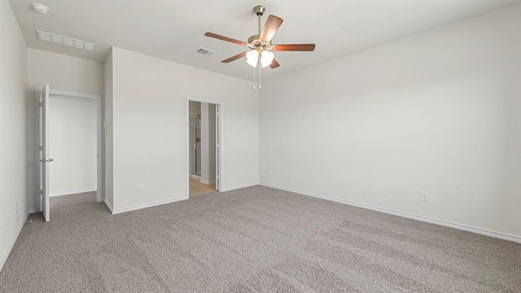 Spacious room featuring neutral carpeting, light-toned walls, and a ceiling fan with wood-finish blades