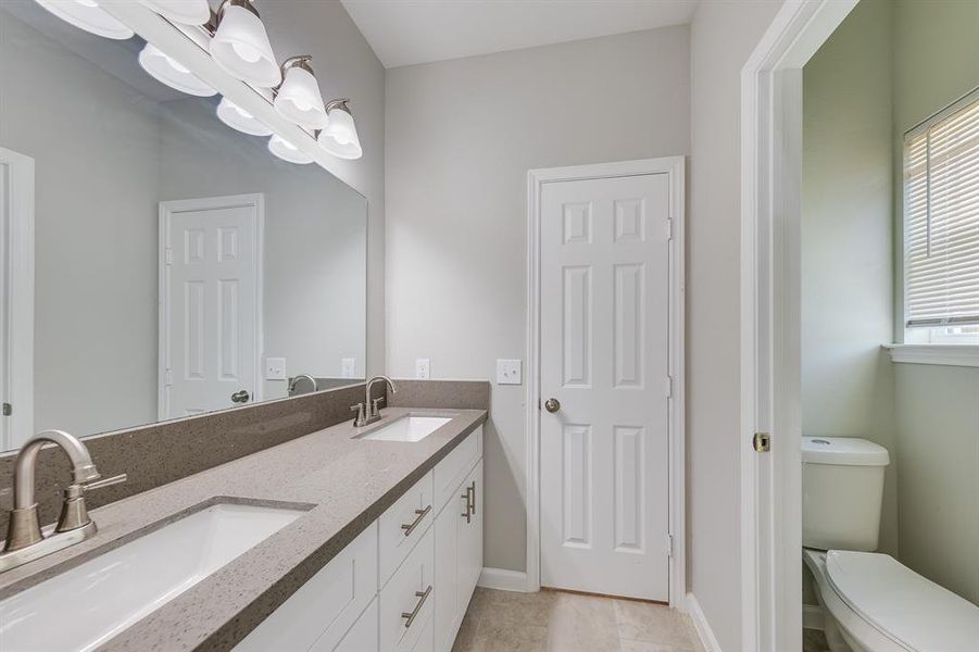 The primary bathroom was designed with luxury and convenience in mind. It features double sinks and a large mirror, perfect for couples or anyone who shares the space. The elegant cabinets beneath provide ample storage, keeping the counters clean and clutter-free for a polished, organized look. Every detail of this bathroom reflects a blend of style and practicality, making it a true retreat within the home.