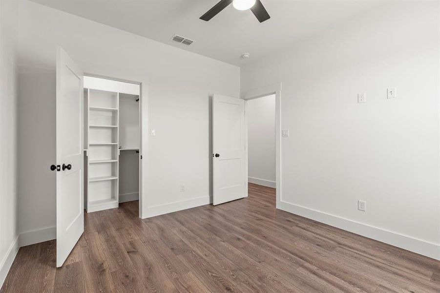 Unfurnished bedroom with dark wood-type flooring, a spacious closet, a closet, and a ceiling fan
