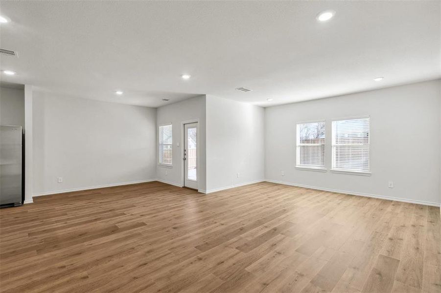 Spacious room featuring wood-finish flooring, two large windows with blinds, recessed lighting, and a rear exterior door