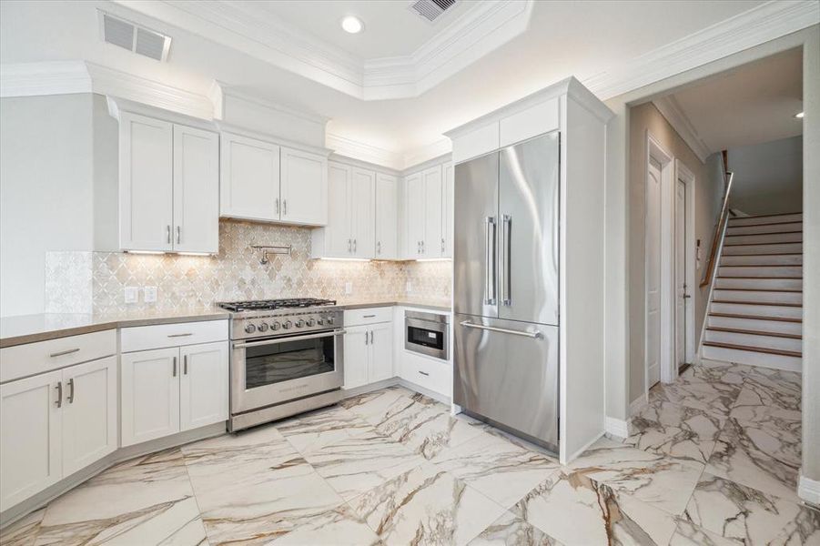 Modern kitchen with white cabinetry, stainless steel appliances, a gas range, and elegant marble flooring extending towards a staircase.