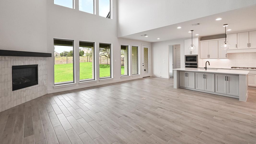 Unfurnished living room featuring light wood-style flooring, a fireplace, a towering ceiling, a sink, and recessed lighting