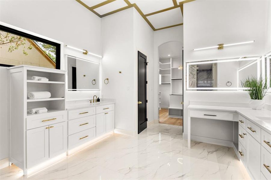 Spacious bathroom featuring white cabinetry with gold-toned hardware, under-cabinet lighting, and large format marble-look floor tiles