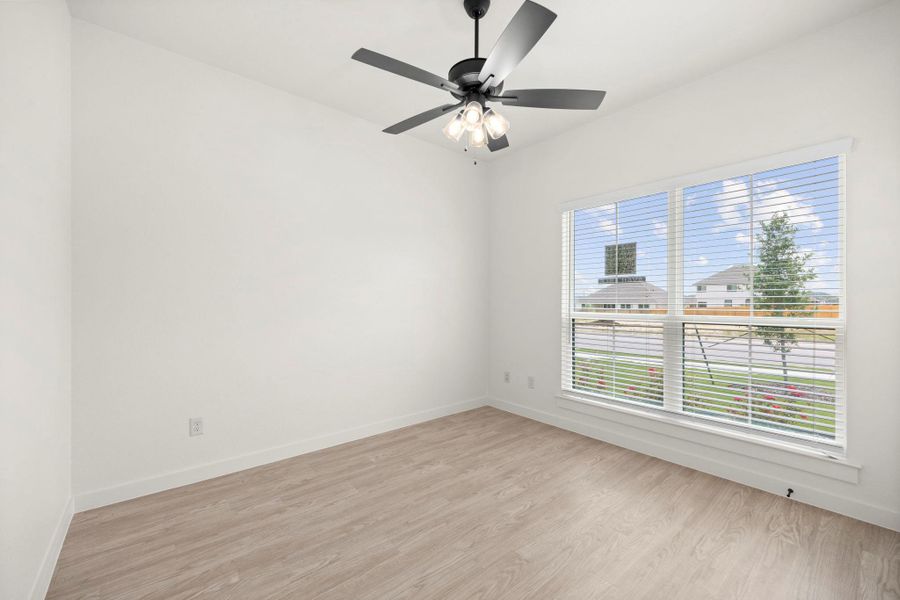 A well-lit bedroom features durable laminate flooring and a functional ceiling fan with lighting.