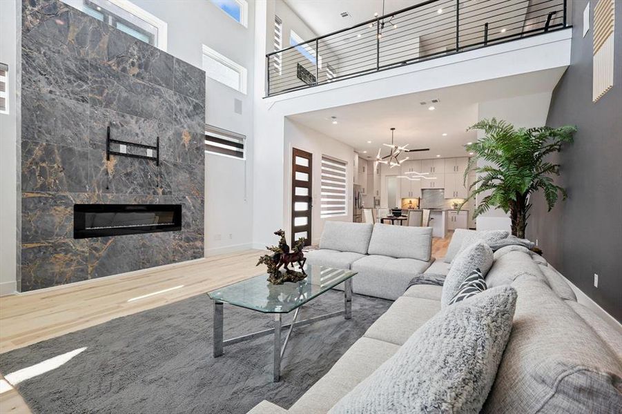 Living room with ceiling fan, wood-type flooring, a high ceiling, and a tiled fireplace