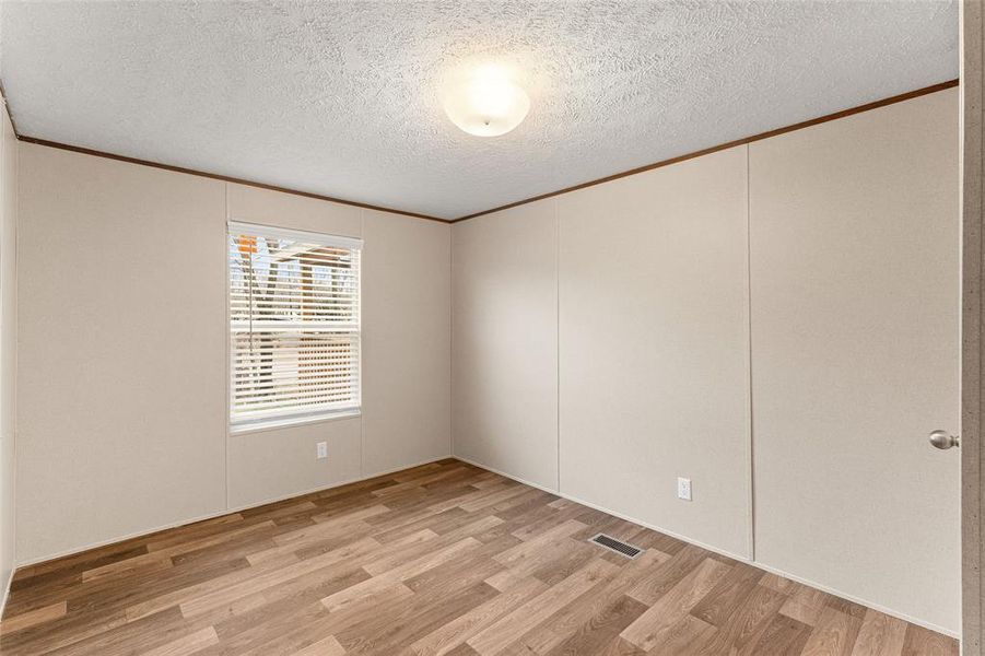Empty room with a textured ceiling, light wood finished floors, and crown molding