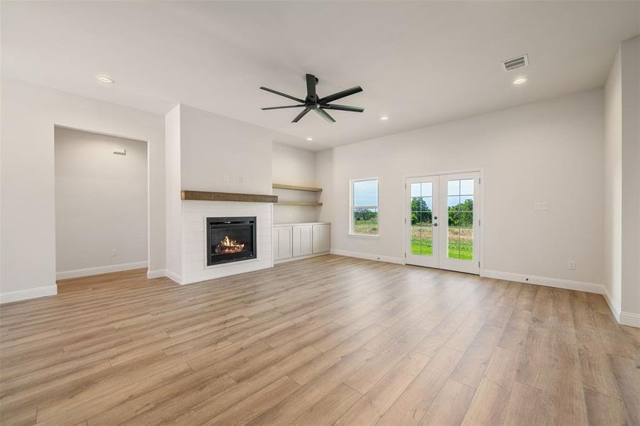 Unfurnished living room featuring ceiling fan, a glass covered fireplace, light wood-style flooring, recessed lighting, and french doors