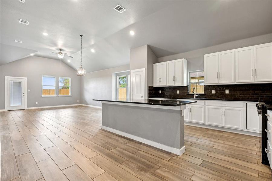 Kitchen with white cabinets, decorative light fixtures, lofted ceiling, ceiling fan, and decorative backsplash