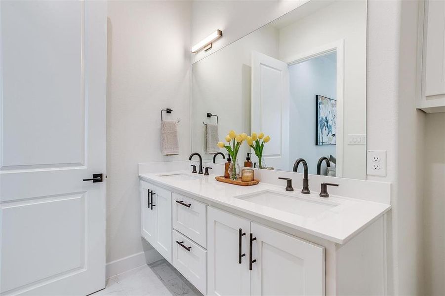 Bathroom featuring double vanity and light marble finish floors Bathroom featuring double vanity and light marble finish floors