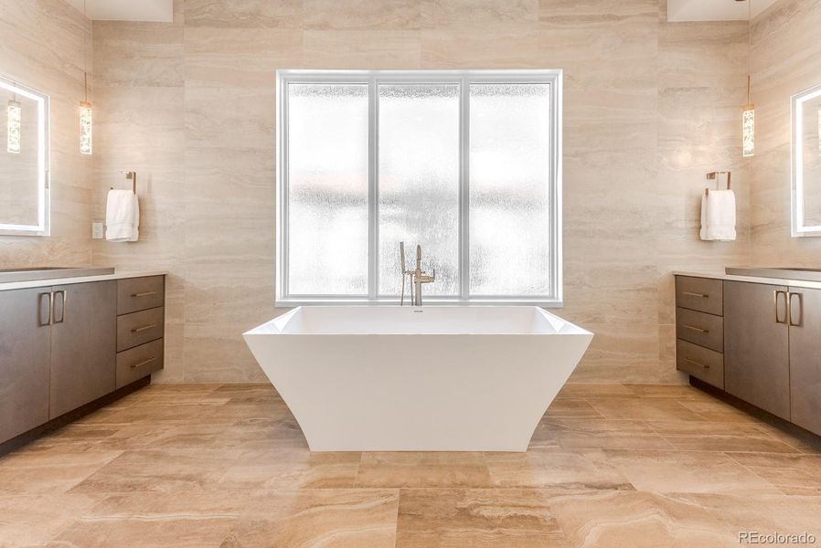 The en-suite bath centers on a freestanding soaking tub positioned before fully tiled walls. Personal vanities feature poured-concrete sinks beneath back-lit mirrors and decorative pendant lighting.