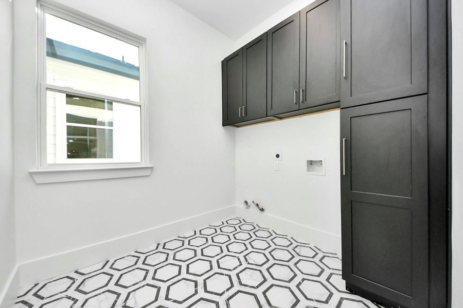 Walk-in, spacious laundry room offering ample storage, highlighted by bold black cabinets, striking hexagon tiles, and a generously sized vanity closet to keep everything organized. Walk-in, spacious laundry room offering ample storage, highlighted by bold black cabinets, striking hexagon tiles, and a generously sized vanity closet to keep everything organized.