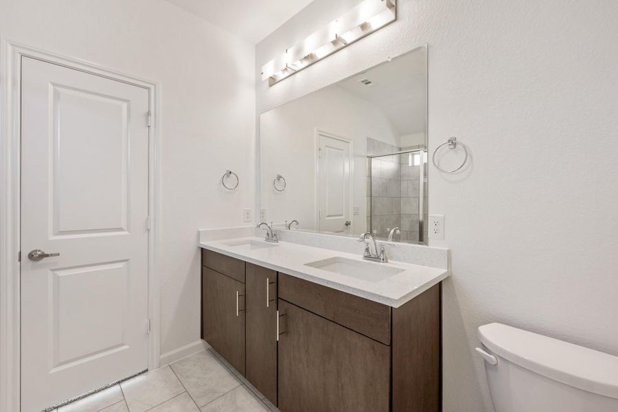 Bathroom with double sink vanity, dark wood cabinets, white countertops, and large mirror with overhead lighting