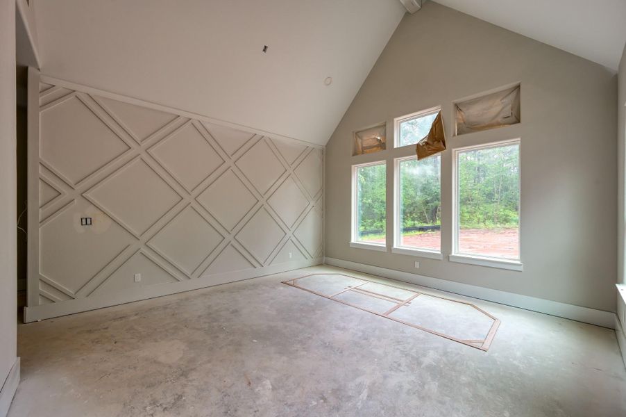 This primary suite features a high ceiling with a stylish geometric accent wall, large windows offering natural light and views of greenery to wake up to.