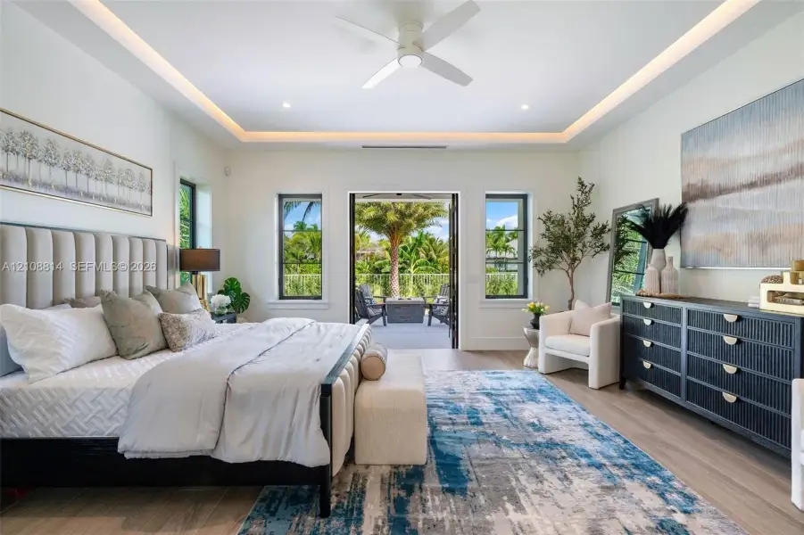 Bedroom featuring a tray ceiling with cove lighting, porcelain-finish flooring, a ceiling fan, and multi-pane windows with glass door access to an exterior area Bedroom featuring a tray ceiling with cove lighting, porcelain-finish flooring, a ceiling fan, and multi-pane windows with glass door access to an exterior area