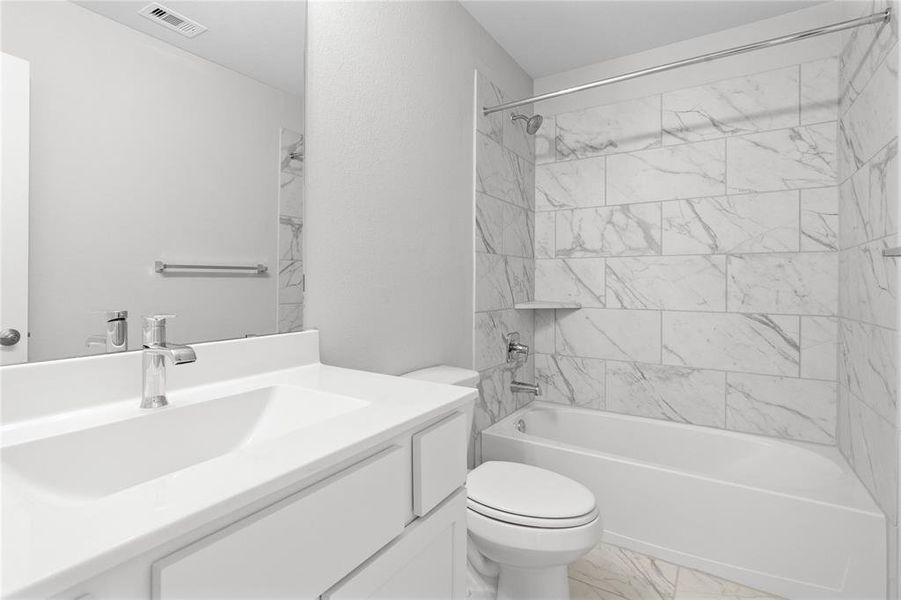 Secondary bath features tile flooring, bath/shower combo with tile surround, white stained wood cabinets, beautiful light countertops, mirror, dark, sleek fixtures and modern finishes.