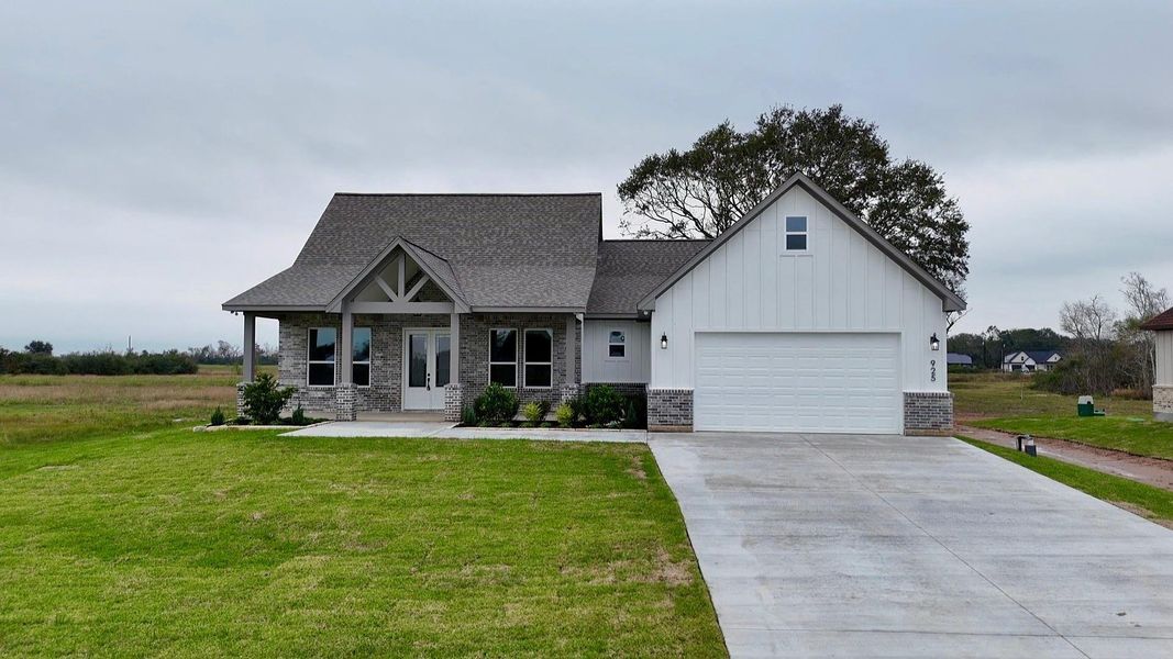 This photo shows a modern single-story home with a gabled roof and a mix of brick and siding exterior. It features a two-car garage, a spacious driveway, and a neatly maintained front lawn. The house is set in a rural area, providing a peaceful, open setting.