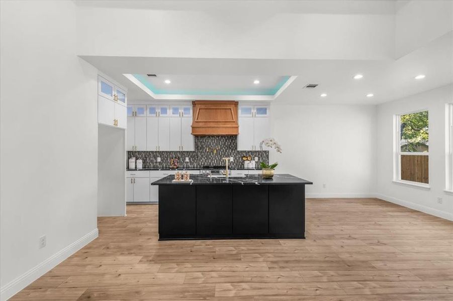 Kitchen featuring decorative backsplash, white cabinets, a raised ceiling, a kitchen island with sink, and recessed lighting