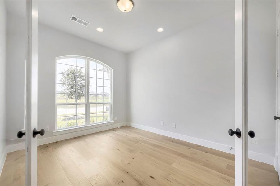Room featuring a large arched window with grid patterns, wood-finish flooring, white baseboards, and recessed lighting