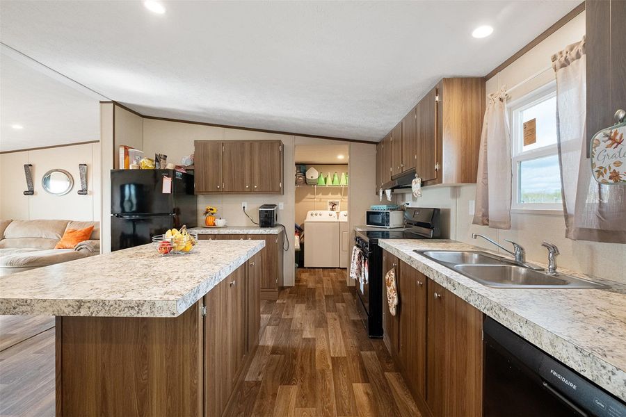 Kitchen featuring dark wood-type flooring, black appliances, a center island, light countertops, and recessed lighting