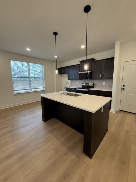 Kitchen featuring hanging light fixtures, stainless steel appliances, a center island with sink, a kitchen bar, and light wood-style flooring